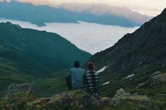 two person sitting on edge of mountain photograph